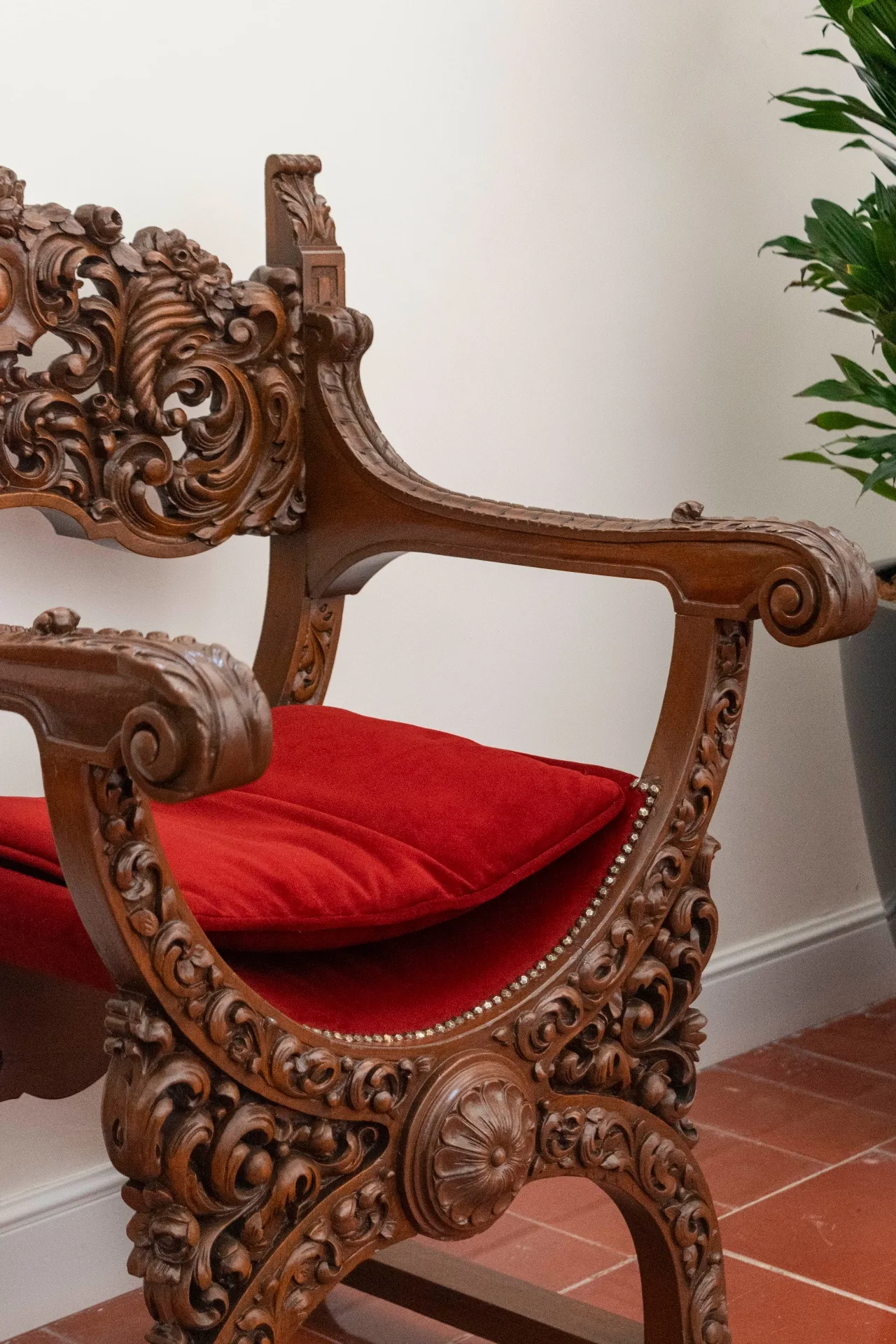 Sillón tallado de madera con cojín rojo en recepción de Casa Lerma